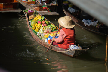 Obraz premium Local fruit vendor rowing a boat at a traditional Thai floating market.