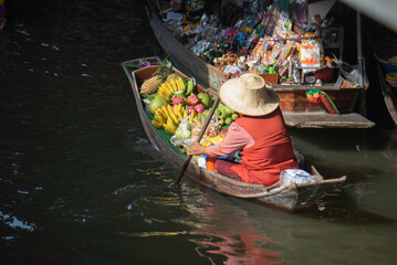 Obraz premium Local fruit vendor rowing a boat at a traditional Thai floating market.