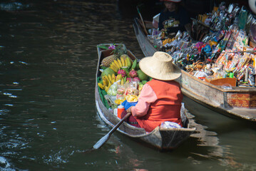 Obraz premium Local fruit vendor rowing a boat at a traditional Thai floating market.