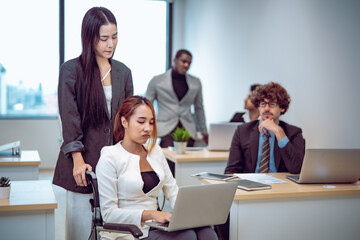 Fototapeta premium Professional workplace scene features employee with disability focused on computer work while colleague stands beside showing encouragement trust inclusion productive business culture