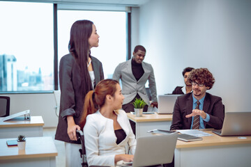 Fototapeta premium Business workplace shows employee with disability working on laptop with serious thoughtful expression while colleague stands behind offering guidance support responsibility teamwork professional.
