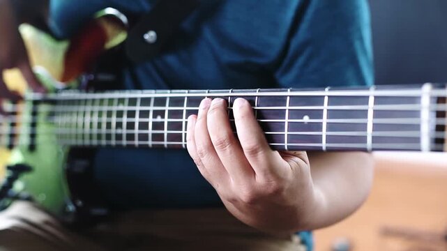 Close-up of bassist playing electric bass guitar in music studio