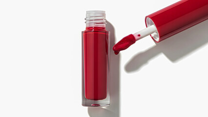 Red lip gloss and applicator on a white background viewed from above