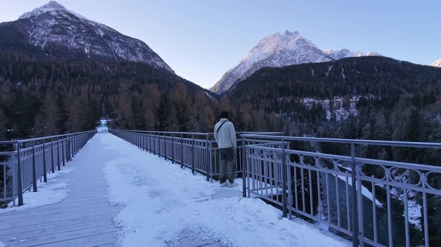 Man Walking Across Icy Bridge in Swiss Alpine Village During Winter &ndash; Snowy Mountains, Rural Switzerland and Cold Seasonal Atmosphere