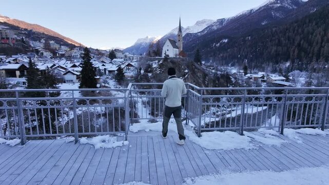 Man Walking Across Icy Bridge in Swiss Alpine Village During Winter &ndash; Snowy Mountains, Rural Switzerland and Cold Seasonal Atmosphere