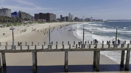 Drone flies north, low over Ku D' Ta Pier on a sunny day along the Golden Mile beach in Durban, South Africa