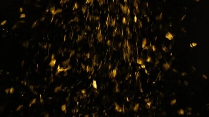 Abstract golden confetti falling down in slow motion against a dark background, creating a festive atmosphere