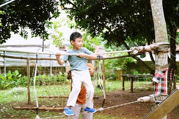 Father supporting his son during a balance activity made from natural materials. Represents trust, learning, resilience, and sustainable outdoor education.