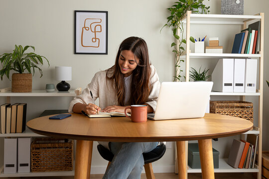 Young happy female caucasian entrepreneur handwriting on a notebook while working at home office - Powered by Adobe