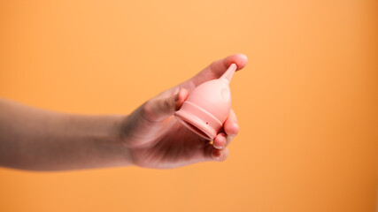 Female Hand Holding Menstrual Cup on Orange Background Minimal Hygiene