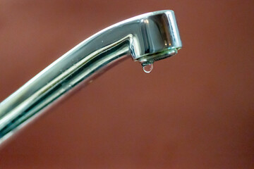 Leaking faucet dripping water, close-up on red background