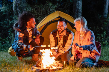 Friends camping at night roasting marshmallows around campfire