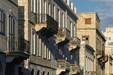 Historic architecture in Ermoupolis, Syros, Greece, featuring a row of stone buildings with wrought...