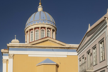 Church of Saint Nicholas in Syros, Greece, featuring a large blue dome topped with a golden cross. The dome sits above a red and white drum with tall arched windows