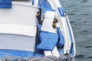 Serene maritime detail in Syros, Greece, showing the front of a small boat floating gently on calm water. The boat is painted white and light blue, with a rope tied to its bow.