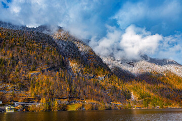 Misty clouds cling to the snow-dusted peaks of the Austrian Alps rising steeply above Lake Hallstatt.