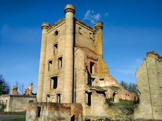 abandoned castle ruins, a dilapidated, tall building with cylindrical towers and ruined windows stands amidst vegetation and clear skies, evoking desolation