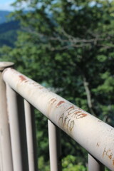 錆びた白い手すりに刻まれた二人の名前と緑の木々のボケ背景｜時間の経過を感じさせる風景と静かな屋外空間