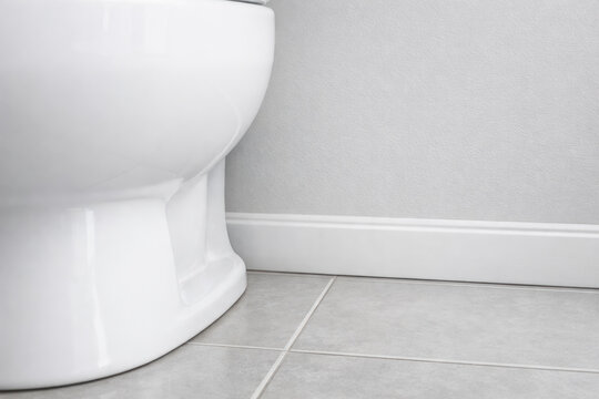 Clean white ceramic toilet base on gray tiled bathroom floor with minimal wall and baseboard detail, modern sanitary interior