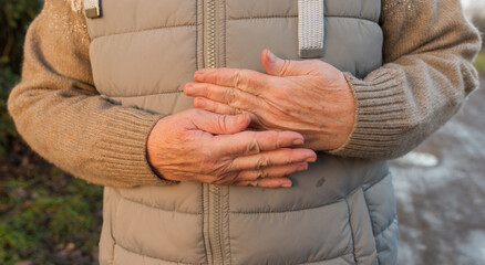 Close-up of mature hands pressed together on a padded vest, suggesting warmth, comfort, and chilly outdoor conditions. Seasonal cold-weather concept for health, winter lifestyle, and cozy clothing pro