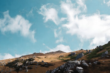 A picturesque landscape displays a rugged rocky hill beneath a vast blue sky