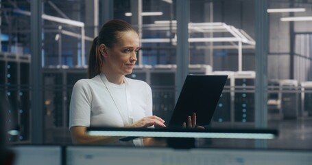 Mobile IT Management, Focused Female IT Professional Standing and Actively Working on Thin Laptop....