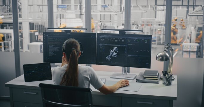 Female Engineer on Headset, Managing 3D Robot Automation Model and Performance Metrics on Monitors. Control Room Overlooks Industry 4.0 Factory Floor. Smart Manufacturing and Robotics Management. - Powered by Adobe