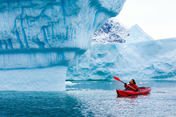 kayak adventure expedition in Antarctica, man paddling on red kayak between icebergs
