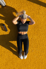 Young woman resting after workout on vibrant yellow outdoor surface