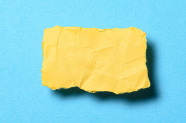 One single yellow torn ripped wrinkled crumpled blank paper note with shadow and copy space for text on light blue background