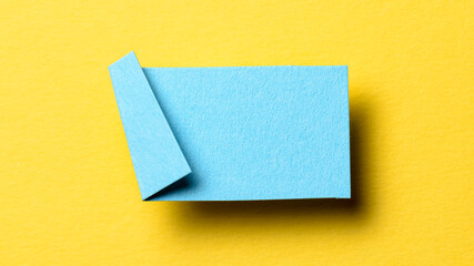 Blue blank paper note cardboard with folded corner dog-ear earmark, shadow and copy space for text on yellow background