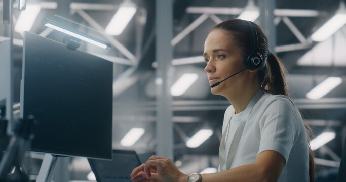 Female Operator Providing Remote Technical Assistance While Speaking on Headset in Setting Modern Enterprise Control Center. Concept of Customer Service, Troubleshooting, and Enterprise Support.