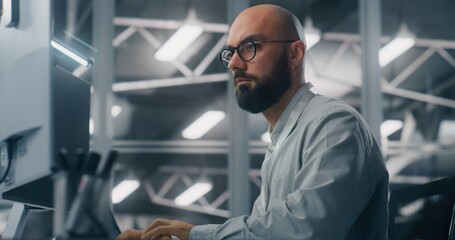 Bearded Male IT Specialist With Glasses, Intensely Focused on Computer Monitor. Background Features Cool, Technical Environment of Server Control Room. Critical Data Analysis and Dedicated Expertise.