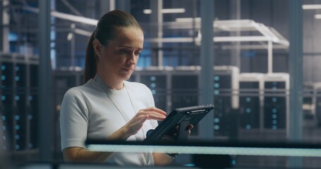 Woman, IT Specialist Stands and Uses Portable Tablet Device to Check Real Time Performance Metrics in High Security Server Hall. Concept of System Monitoring, on Site Expertise, and Data Analysis.
