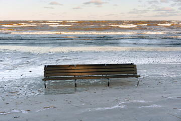 Lonely Wooden Bench on a Sandy Beach with Sea Waves and Clouds