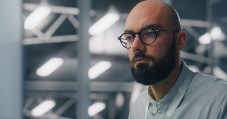 Close Up of Dedicated Engineer Oversees Digital Infrastructure From Workstation. Blue Lit, High Security Data Center Environment Visible in Soft Focus. Professional Monitoring and Technical Expertise.