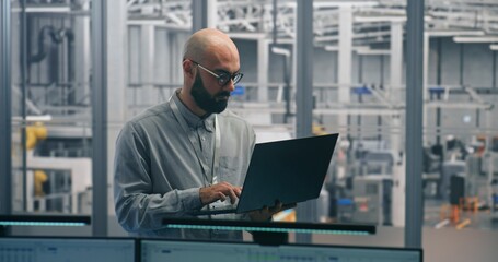 Engineer Tracking Production Process With Laptop. Experienced Male Specialist Auditing Production Flow and Metrics on thin laptop. Engineering Oversight, Digital Tools in Smart Manufacturing.