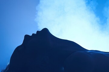 Sensual silhouette of a woman's profile against blue light and atmospheric smoke.