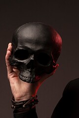 Close up of a hand holding a matte black human skull prop with dramatic red accent light