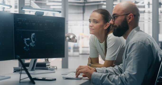 Focused Specialists Monitoring Factory Automation Work. Male and Female Technical Specialist Monitoring Real Time Factory Automation on Dual Screen Workstation. Process Control, Technical Oversight.