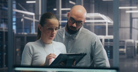 Male and Female IT Engineer Team Collaborating and Discussing Data Displayed on Digital Tablet, Standing in Secure, High Tech Environment of Data Center. Concept Teamwork and Mobile System Diagnostic.