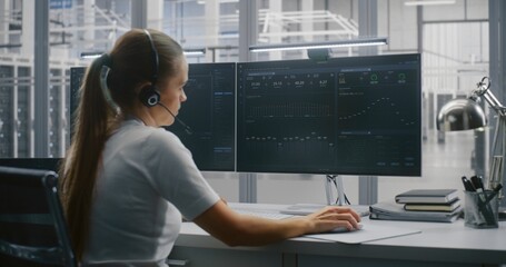 Young Female Professional Manages Large Servers Operations From Modern Workstation. Woman Wears Headset For Active Communication. Technological Innovation, Diverse Workforce and Innovative Workplace.