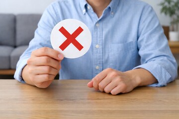 机に座る男性がバツ印カードを提示して否定や不正解を示す判断と意思決定のシーンイメージ