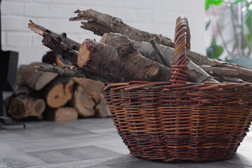 Wicker Basket with Firewood near Fireplace in a cozy home interior. Stacked logs in the background. Winter heating rustic lifestyle concept.