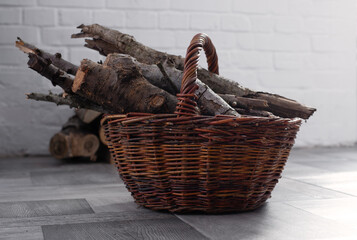 Wicker Basket with Firewood near Fireplace in a cozy home interior. Stacked logs in the background. Winter heating rustic lifestyle concept.