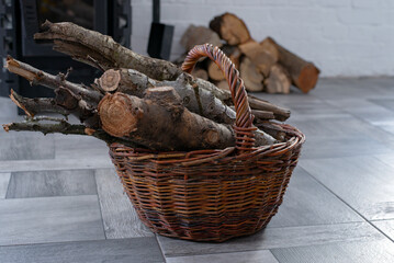 Wicker Basket with Firewood near Fireplace in a cozy home interior. Stacked logs in the background. Winter heating rustic lifestyle concept.
