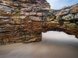 Natural rock formation arching over sandy beach in Nazar&eacute;, Portugal