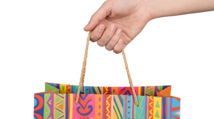 Hand holding colorful patterned paper shopping bag with rope handles isolated on transparent background