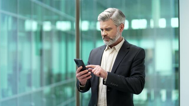 Worried businessman having problems with software or service on smartphone mobile phone standing in business office. Frustrated disappointed mature worker complains about bad internet connection