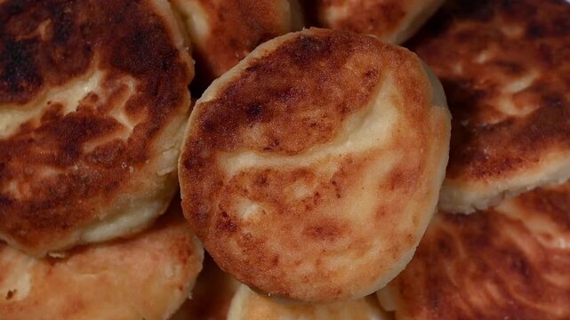 A seamless 4K video loop of golden-brown cottage cheese pancakes (syrniki) rotating on a decorative plate, filmed from a top-down perspective. The clip highlights their appetizing texture, slight cris
